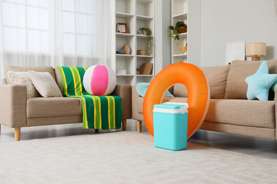 Living room with summer vacation items including a beach ball, inflatable ring, and cooler, ready for travel