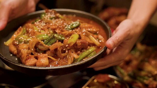 Close Up of Hands Holding Spicy Korean Pork Stir Fry Dish