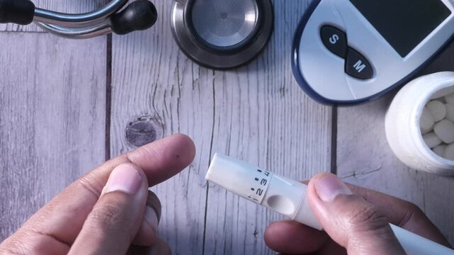 Person using lancet device to prick finger for blood glucose test on wooden background with medical equipment