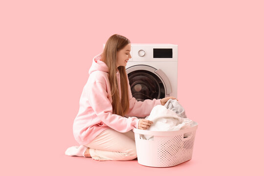 Pretty young woman enjoying clean clothes near washing machine on pink background