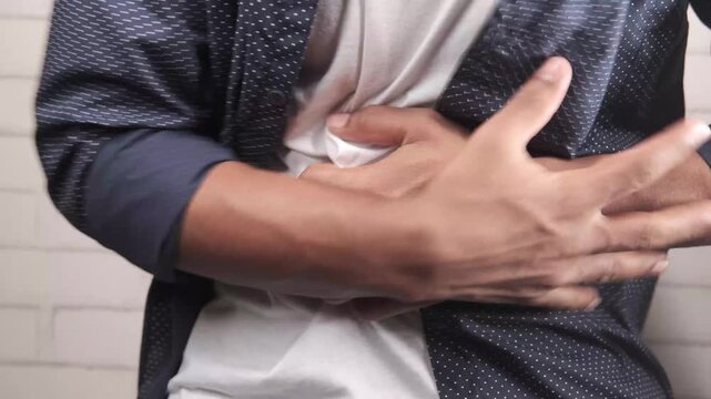 Close up video of young man suffering from stomach ache, holding his painful belly and grimacing in discomfort