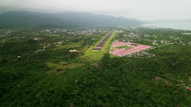 Panoramic aerial view of lone airport runway amid lush tropical island greenery and residential homes - Virac Airport, Catanduanes, Philippines