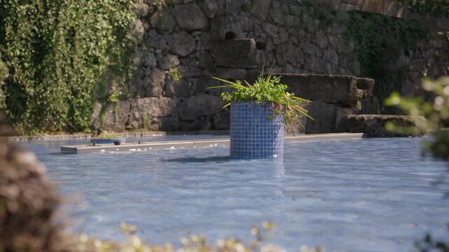 Blue mosaic tiled planter with plants rising from a pool beside a stone wall
