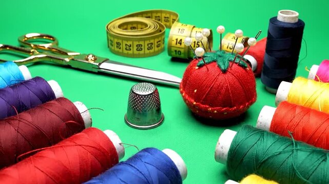 Colorful sewing thread spools and tailoring tools on green background