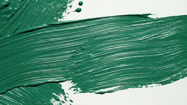 Close up footage of a paintbrush applying thick emerald green paint with textured strokes on a white surface, creating artistic designs