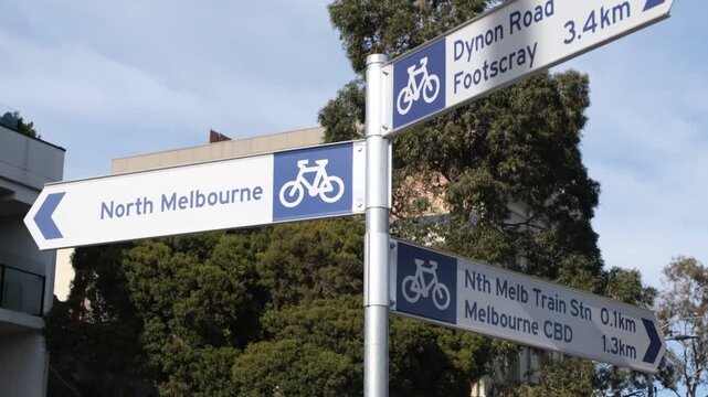 Directional cycling wayfinding sign pointing towards North Melbourne, Footscray, and CBD in Melbourne Australia, multi-storey residential buildings form the background&nbsp;