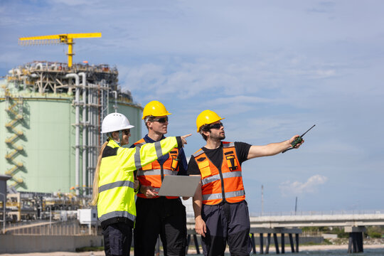Engineers team pointing and planning at LNG plant facility, Refinery technicians collaborating at natural gas terminal site, Worker team in safety gear discussing operations at industrial plant