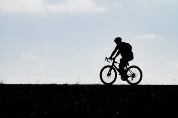 Obraz premium A stark profile silhouette of a cyclist wearing a helmet riding a bicycle along a hill horizon showcasing outdoor fitness healthy sport cycling commuting and endurance activity under an open sky.