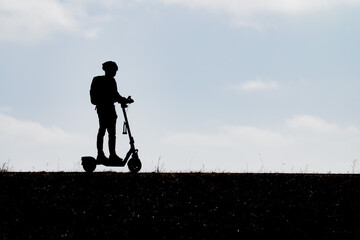 Modern silhouette of a person wearing a helmet and riding an electric scooter along an elevated path against a bright sky capturing eco-friendly urban mobility active travel and micro-transit. © William Toy