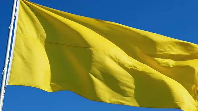 Yellow flag waving against a clear blue sky, representing caution or a warning, movement and freedom