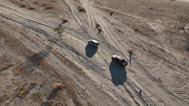 Overhead Aerial Tracking Shot of Off-Road Vehicles Driving on a Sandy Trail with Long Shadows