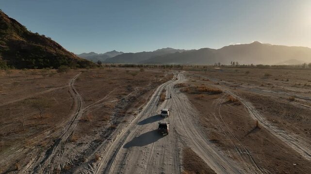 Aerial Tracking Shot of Off-Road Vehicles on a Dusty Lahar Trail at Sunset