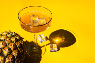 Refreshing pineapple cocktail with ice cubes on a bright yellow summer background. © baramyou0708