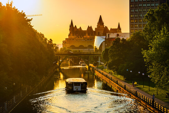 Ottawa, ON, Canada. July 20, 2026. A tour boat sails down the Rideau Canal toward Ch&acirc;teau Laurier during a golden sunset.