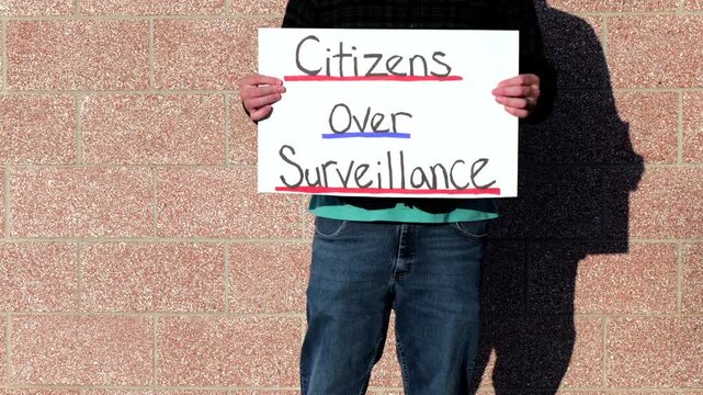 Demonstrator holding a Citizens Over Surveillance sign, protesting mass tracking, license plate readers, Fourth Amendment overreach illegal search