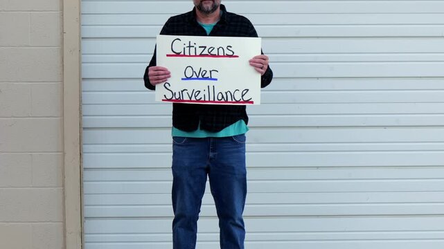 Demonstrator holding a Citizens Over Surveillance sign, protesting mass tracking, license plate readers, Fourth Amendment overreach illegal search
