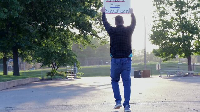 Demonstrator holding a Citizens Over Surveillance sign, protesting mass tracking, license plate readers, Fourth Amendment overreach illegal search