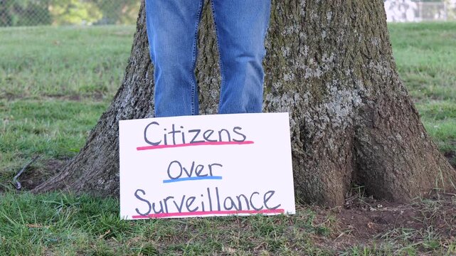 Demonstrator holding a Citizens Over Surveillance sign, protesting mass tracking, license plate readers, Fourth Amendment overreach illegal search