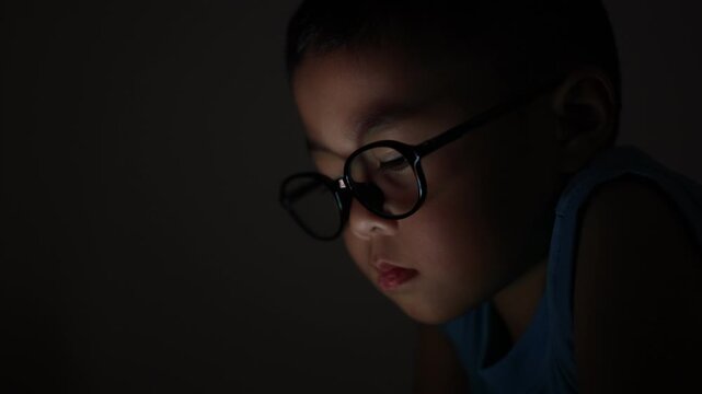 The little boy is using a smartphone at home at night. Closeup of a little boy face in night, using phone, technology concept