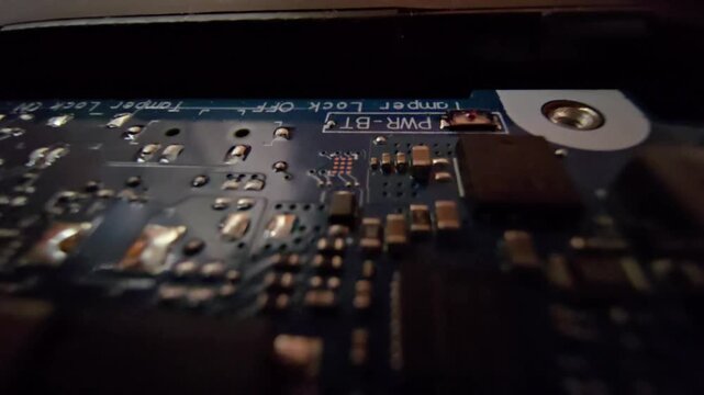Detailed macro shot of a blue circuit board displaying silkscreen markings such as "PWR-BT" and "Tamper Lock OFF" alongside various surface-mounted resistors and capacitors.