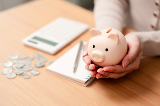 Financial security and saving money concept. Woman hands holding a piggy bank with coins and calculator on desk.