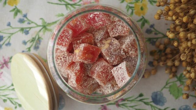 A mesmerizing overhead shot of red turkish delight in a jar with the lid taken off, showing the candy's texture, dynamic camera movement