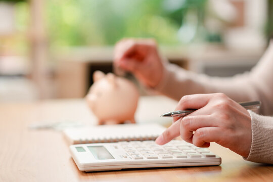 Personal finance and home budgeting concept. Woman calculating expenses and putting a coin into a piggy bank.