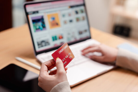 Online shopping and digital payment concept. Hand holding a red credit card while typing on laptop keyboard.