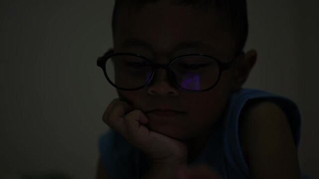 The little boy is using a smartphone at home at night. Closeup of a little boy face in night, using phone, technology concept