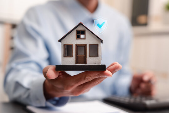 Property insurance and home protection concept. Businessman holding a model house with a digital shield and checkmark icon.