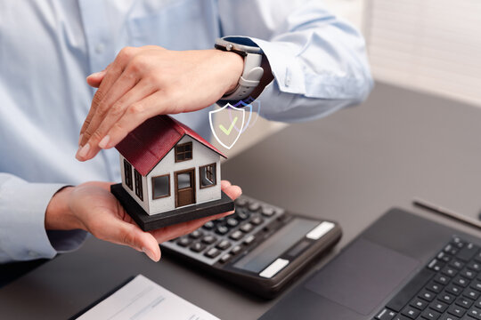 Property insurance and home protection concept. Businessman hands protecting a model house with shield icons and checkmark.