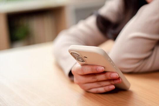 Woman hands holding and using a smartphone on a wooden table. Modern digital lifestyle and communication concept.