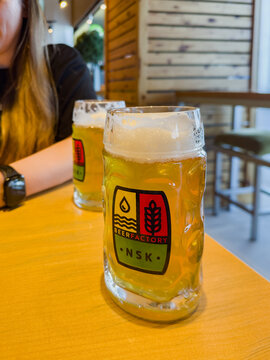 Two glass mugs of cold draft beer with foam and Beer Factory NSK logo on table at Tolmachevo Airport lounge in Novosibirsk, Russia - July 21, 2026
