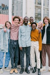 Fototapeta premium Diverse group of young adult friends standing together and smiling on an urban street with reflecting windows for lifestyle branding