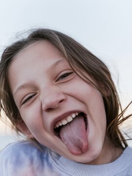 Young girl laughing and sticking out her tongue in a playful candid expression for family lifestyle and childhood humor content