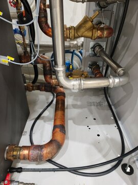A vertical shot of complex copper and stainless steel piping connected inside an industrial machine cabinet