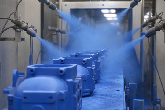 Inside a spray booth, products on a conveyor belt passing through atomized colored powder.