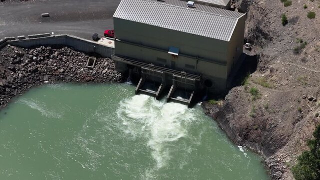 Aerial of Tieton dam and river with industrial building in Washington with spillway gates releasing water into a downstream river channel