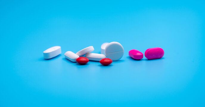 White and pink tablets pill spread on blue background with copy space. Pharmacy web banner. Pharmaceutical industry. Round and oval tablets pills. Prescription drugs. Sample pills for clinical trial.