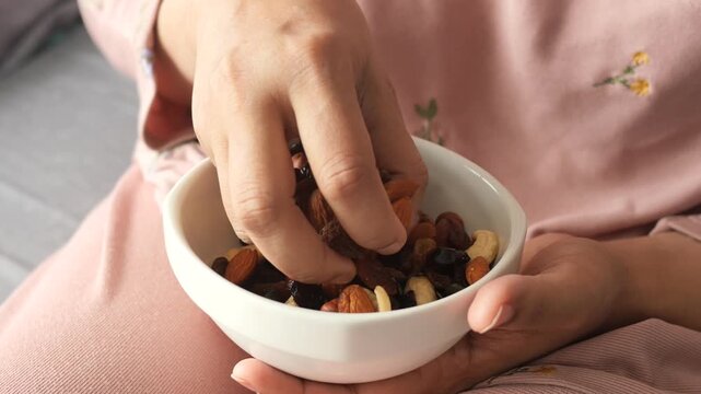 Woman's hands hold and pick up a bowl of nutritious trail mix containing various nuts and dried fruits