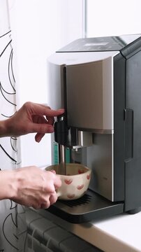 Vertical video. Drink preparing. Making coffee. Female hands using automatic espresso machine for fresh morning beverage at home kitchen.