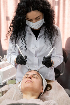 Cosmetician working. Aesthetic therapy. Female in black gloves using professional device for modern facial microcurrent procedure.