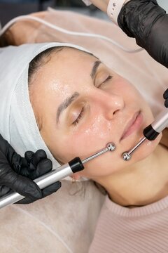 Woman treatment. Microcurrent procedure. Professional cosmetologist hands in black gloves using device for facial skin lifting.