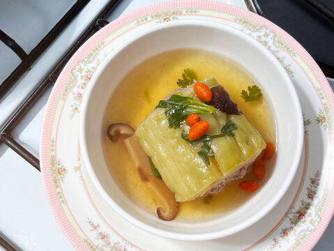 Top view healthy Thai stuffed bitter gourd soup with minced pork, shiitake mushroom, and goji berries in a white bowl. Perfect for Asian herbal home cooking and wellness food.
