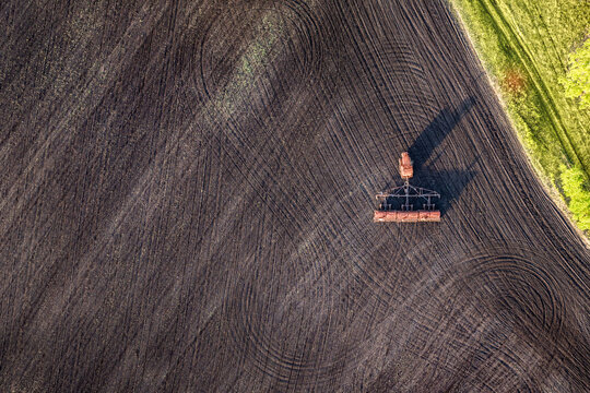 Seeding equipment working on plowed agricultural field with copy space, soil preparation and planting operations on farmland, aerial view of farming, crop production and arable land