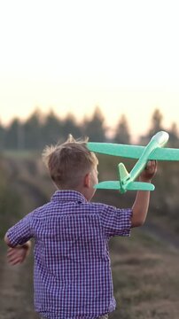 Happy little kid running with a green toy airplane in a rural field during sunset, dreaming of becoming a pilot and enjoying a carefree childhood on a summer evening