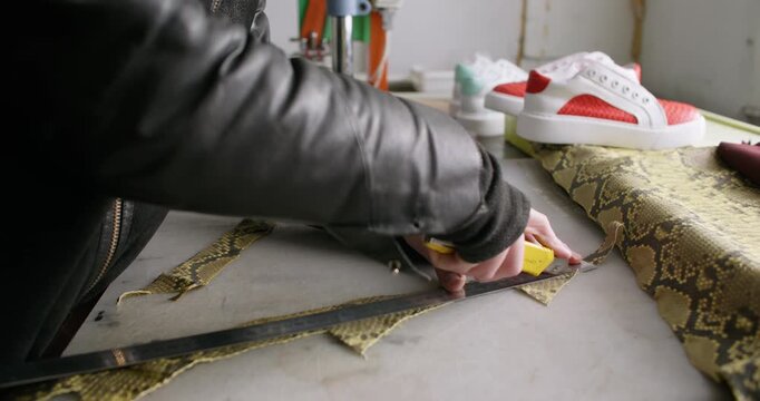 Shoe craft. Leather workshop. Unrecognizable professional man hands using stationery knife metal ruler cutting material at workplace.