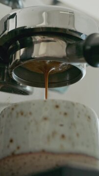 Close up of espresso extraction from bottomless portafilter into white cup.