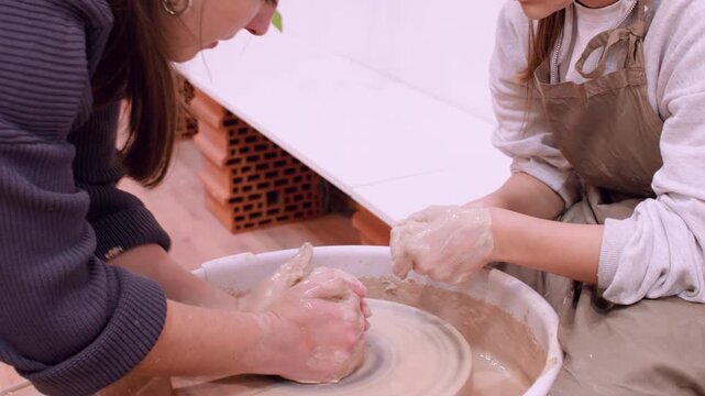 Artisan lesson. Clay modeling. Professional woman specialist teaching talented girl handmade craft using electric wheel in workplace.