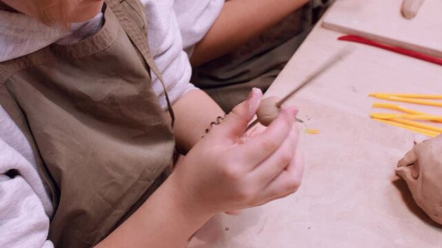 Diy craft. Artisan master class. Creative unrecognizable kids hands shaping ceramic molding raw clay using color tool in professional art studio.